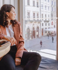 A person sitting by a window in a café, overlooking a city street scene with buildings in the background.
