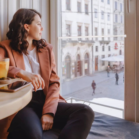 A person sitting by a window in a café, overlooking a city street scene with buildings in the background.