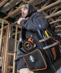 Worker carrying Heavy Duty Tool Bag With Shoulder Strap And 40 Pockets In Bright Orange Interior For Fast Tool Access, Molded Bottom For Stability, Pro Grade Durable Organizer For Contractors And Do It Yourself Projects on construction site