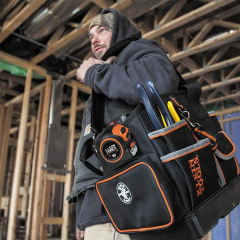 Worker carrying Heavy Duty Tool Bag With Shoulder Strap And 40 Pockets In Bright Orange Interior For Fast Tool Access, Molded Bottom For Stability, Pro Grade Durable Organizer For Contractors And Do It Yourself Projects on construction site