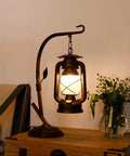 Rustic Lantern Table Lamp with Glass Shade for Living Room and Bedroom Cozy Nightstand Lighting for End Tables Farmhouse Style Bedside Lamp that Delivers Warm Homey Vibe, lit on wooden table next to flowers.