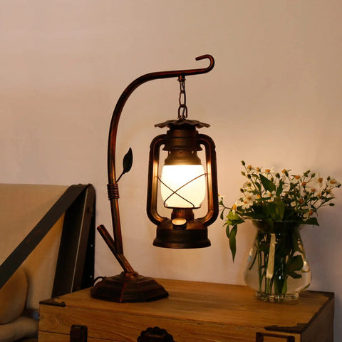 Rustic Lantern Table Lamp with Glass Shade for Living Room and Bedroom Cozy Nightstand Lighting for End Tables Farmhouse Style Bedside Lamp that Delivers Warm Homey Vibe, lit on wooden table next to flowers.