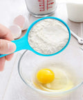 Hand holding blue cup from 12 Piece Measuring Cups And Spoons Set Colorful Kitchen Tools For Quick Prep over bowl with egg