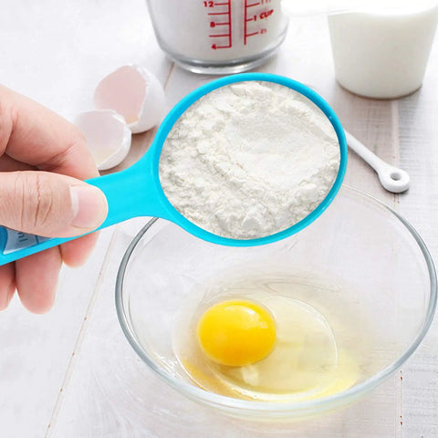 Hand holding blue cup from 12 Piece Measuring Cups And Spoons Set Colorful Kitchen Tools For Quick Prep over bowl with egg