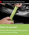 Person unwinding green high-strength automotive masking tape near car, 36mm by 32m, showing conformable backing for easy masking.
