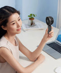 Person using Black fan from Four Pack USB Rechargeable Mini Handheld Fans Set With 3 Speeds, Portable Personal Fans at desk.