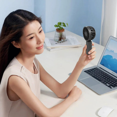 Person using Black fan from Four Pack USB Rechargeable Mini Handheld Fans Set With 3 Speeds, Portable Personal Fans at desk.