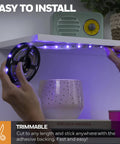 Hands installing Color Changing RGB LED Strip Light 16.4 Ft With Motion Sensor And Remote under a shelf with adhesive backing.