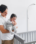 Man holding baby near crib with Floor Stand For Nanit Pro Baby Monitor With Gooseneck Swivel Holder visible in background.