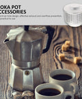 Aluminum mocha pot with spout cover beside two filled espresso cups on wooden table.