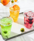 Three 16 oz clear plastic cups with lids on tray, filled with colorful iced drinks, showcasing 50 pack for iced coffee and cold drinks.