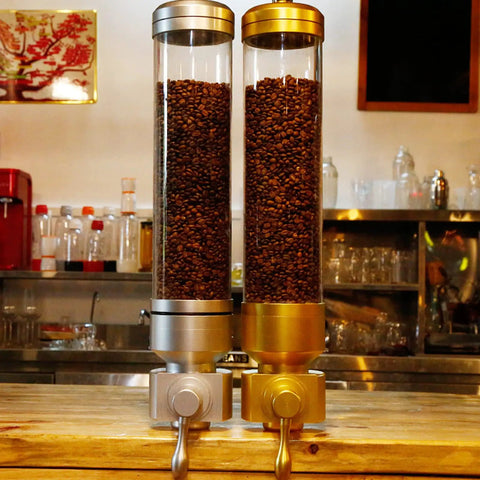 Wall Mounted Transparent Coffee Canister With Gold Trim And Smooth Grip Handle Straight Up Fantastic Dry Food Dispenser For Sugar Rice Nuts Cereals Pet Treats Zero Stress Counter Organizer To Keep Your Pantry Legit with coffee beans inside.
