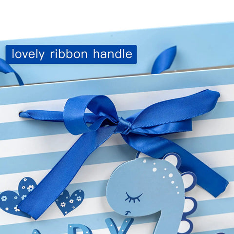 Close-up of Blue Dinosaur Baby Boy Gift Bag With Tissue Paper And Greeting Card Durable Ribbon Handles And Reinforced Bottom 13 By 10 By 5 Inches Perfect For Baby Showers New Parents And More, featuring a blue ribbon handle and dinosaur design.