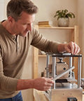 Side view of a man in a beige shirt adjusting a benchtop metal press in a home workshop