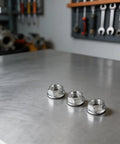 Secure Fit 12mm E-Bike Hub Motor Nuts Safety Washer Steel Locking Hardware For Premium Copper Anodized Bike Parts That Keeps Your Ride Tight And Safe From Vibrations Without Hassle., three steel 12mm locking nuts with washers on a workbench