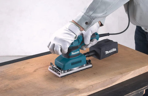 Person using Beast Of A Sheet Finishing Sander One Third Inch Orbit, 1.7 Amp, Teal Finish With Ergonomic Rubberized Grip on wood surface.