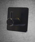 Rock Solid Black Stainless Steel Adhesive Wall Hook For Coats Towels And Umbrellas With No Hassle Peel Stick Mount Zero Drill Setup And Slick Modern Design For Bathrooms And Hallways, showcased on a textured background.