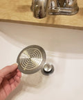 Bathroom Sink And Tub Hair Catcher 2 Pack Non Slip Drain Protector Anti Clog Filter held above sink.