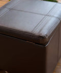 Square brown leather ottoman with stitching details on a wooden floor, closed lid