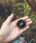 Close-up of a hand holding a compass from the Emergency Sleeping Bag With Compass 2 Pack Portable Waterproof Bivy Sack Blankets Lightweight Survival Gear For Camping Hiking And Outdoor Adventures Today.