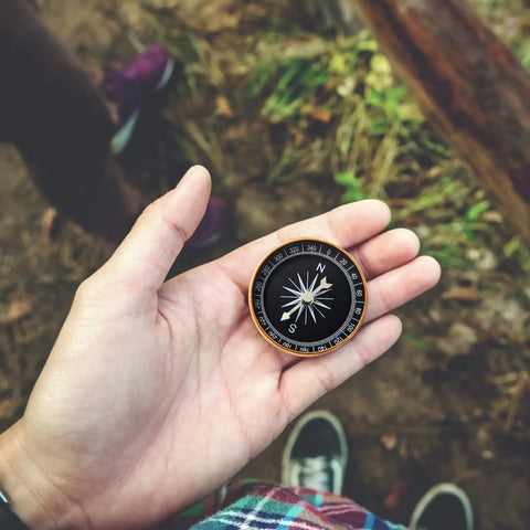 Close-up of a hand holding a compass from the Emergency Sleeping Bag With Compass 2 Pack Portable Waterproof Bivy Sack Blankets Lightweight Survival Gear For Camping Hiking And Outdoor Adventures Today.