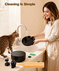 Woman cleaning Wireless Cat Water Fountain Cordless No Cords Needed Battery Operated 88 Oz Black Pet Water Dispenser with cat watching