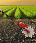 Manual Garden Push Seeder With 7 Nozzles And Eight Pound Seed Box in use on soil, side view, red machine with black handles