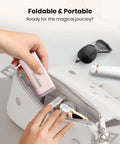Hand placing Airplane Phone Holder Mount for Travel Must Haves in white bag, foldable and pink, with sunglasses and lipstick nearby.