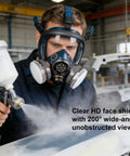 Worker wearing full face gas mask respirator with active carbon filter, using spray gun, industrial environment, safety gear