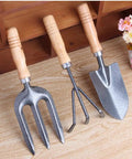 Three Kinds Of Gardening Tools Set Featuring Hooked Mattock Hand Shovel And Trident For Everyday Garden Work And Shoreline Shell Collecting On Tide Flats Built With Iron Heads And Wooden Handles In A Durable Black Finish on wooden surface