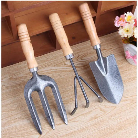 Three Kinds Of Gardening Tools Set Featuring Hooked Mattock Hand Shovel And Trident For Everyday Garden Work And Shoreline Shell Collecting On Tide Flats Built With Iron Heads And Wooden Handles In A Durable Black Finish on wooden surface