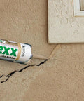 Applying Mor-Flexx Gray Acrylic Latex Caulk For Mortar, Stucco, And Grout Repair to cracked stucco wall near a window.