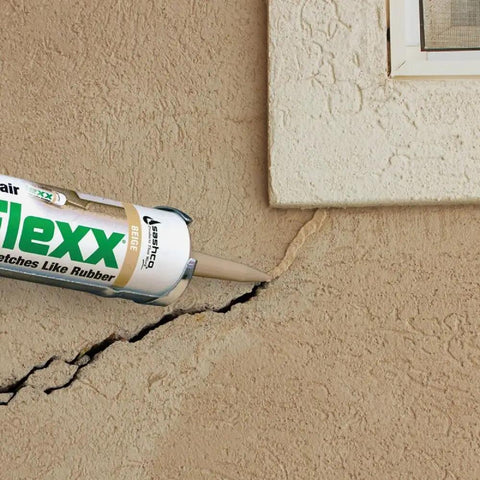 Applying Mor-Flexx Gray Acrylic Latex Caulk For Mortar, Stucco, And Grout Repair to cracked stucco wall near a window.
