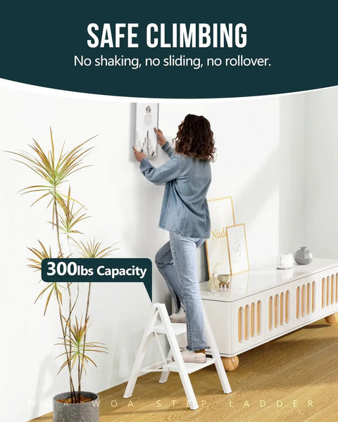 Sturdy 2 Step Ladder With 17 Inch Top Step, 300 Lb Capacity, White Finish, Wider 7.9 Inch Treads For Comfort And Stability, Great For Home, Garage, And DIY Tasks. woman standing on white 2-step ladder hanging wall art indoors