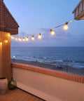 Two Pack 100 Foot Outdoor String Lights With Dimmable G40 LED Bulbs That Are Shatterproof And Weatherproof End To End Connectable Up To Nine Times 100 Feet on a seaside patio at dusk