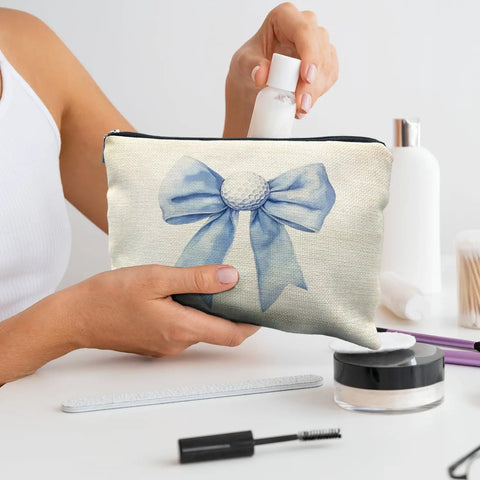 Woman placing a small bottle into a Golf Themed Makeup Bag For Women, Blue Golf Ball Bows Cosmetic Pouch, on a table with cosmetics.