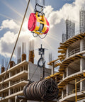 Front view of yellow and red electric hoist winch lifting a coil of steel cable at a construction site