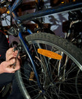 Person installing a bike brake near a wheel with reflectors. Focus on spoke reflectors for night riding safety on mountain and road bikes.