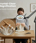 LED Magnifying Floor Lamp With Dual Bifocal Lenses 2.25x And 6x in use by woman knitting at desk, showing stitch details.