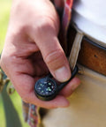 Person holding Liquid Filled Carabiner Compass For Hiking And Camping Lightweight And Compact Navigation Tool clipped to belt