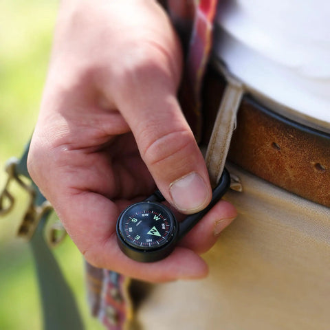 Person holding Liquid Filled Carabiner Compass For Hiking And Camping Lightweight And Compact Navigation Tool clipped to belt