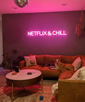 Living room with 'Netflix & Chill' pink neon sign above brown couch and coffee table