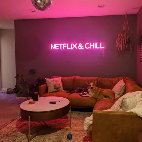 Living room with 'Netflix & Chill' pink neon sign above brown couch and coffee table