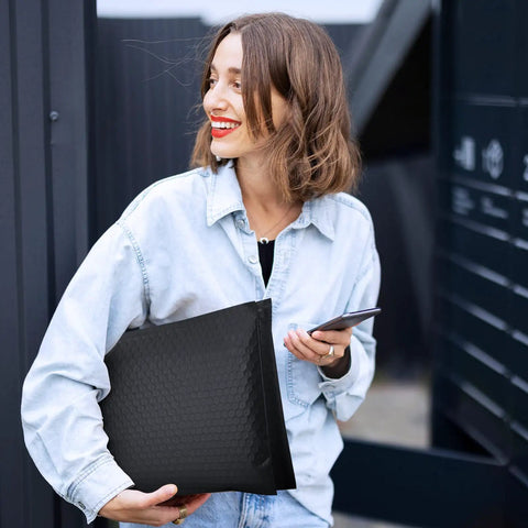 Woman holding 10 Point 5X16 Inch Bubble Mailers 40 Pack Self Seal Padded Envelopes Waterproof Cushioning Mailers, in a black design outdoors