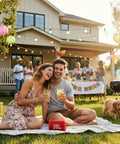 Outdoor party with people relaxing on a blanket in a garden, featuring a red JBL portable speaker, decorative lights, and food table.
