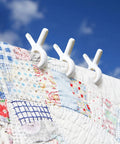 White plastic clips from 12 Pack Heavy Duty Plastic Clothes Pins Featuring Anti Rust Springs And Non Slip Silicone Pads holding a quilt.
