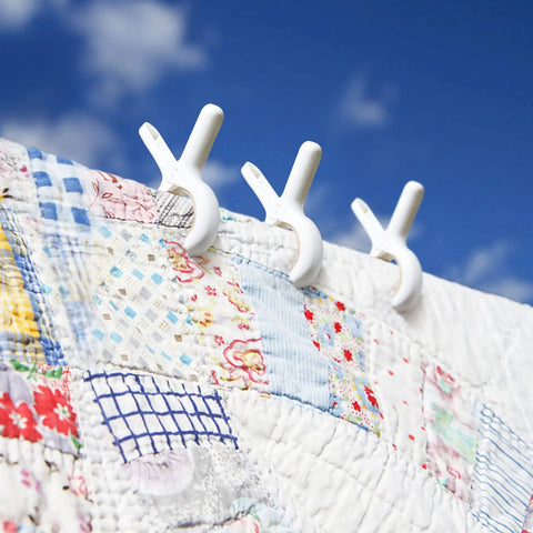 White plastic clips from 12 Pack Heavy Duty Plastic Clothes Pins Featuring Anti Rust Springs And Non Slip Silicone Pads holding a quilt.