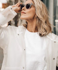 Person wearing transparent raincoat, snapping fasteners, sunglasses, and white shirt outdoors