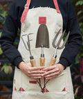 Person holding 3 Piece Garden Tool Set With Stainless Steel Hand Trowel Hand Cultivator And Hand Fork With Wood Handles in garden.