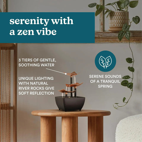 Tabletop Water Fountain With Three Tiers For Indoor Zen Waterfall Vibe, placed on a wooden table, with river rocks and plants nearby.